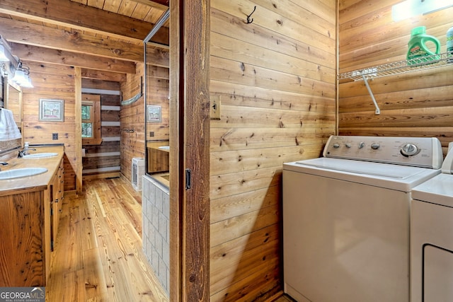 washroom with laundry area, wooden walls, washer and clothes dryer, light wood-type flooring, and a sink