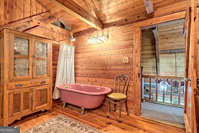 bathroom with wooden walls, lofted ceiling with beams, wood ceiling, wood-type flooring, and a freestanding bath