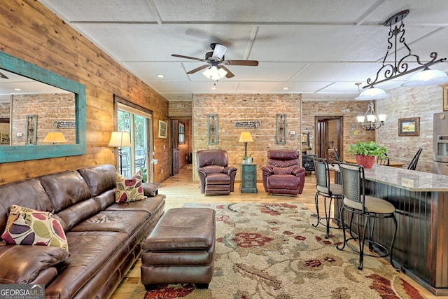 living room with light wood finished floors, brick wall, and ceiling fan with notable chandelier