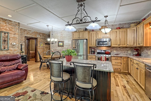 kitchen with appliances with stainless steel finishes, light wood-type flooring, a kitchen island, and light stone countertops