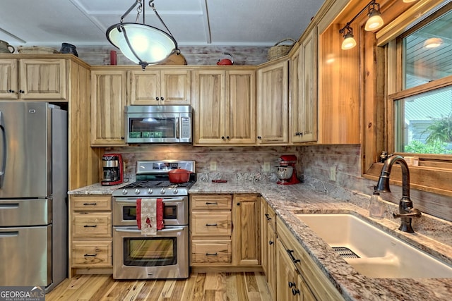 kitchen featuring light wood-style flooring, a sink, appliances with stainless steel finishes, light stone countertops, and tasteful backsplash