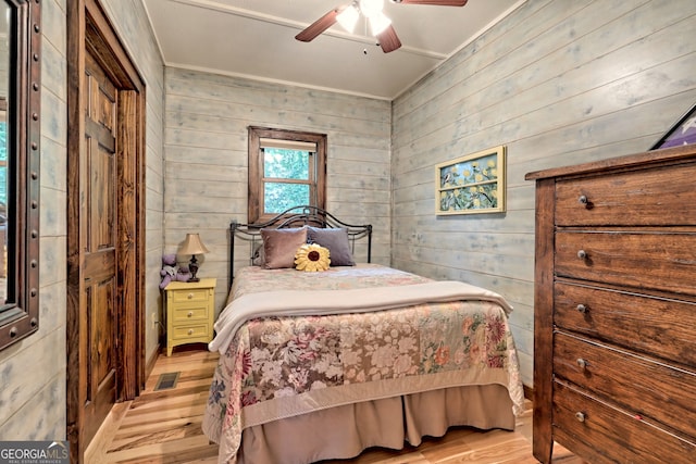 bedroom with a ceiling fan, visible vents, wooden walls, and light wood finished floors