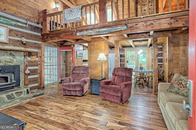 living room with a towering ceiling, hardwood / wood-style flooring, wood ceiling, a wood stove, and wood walls