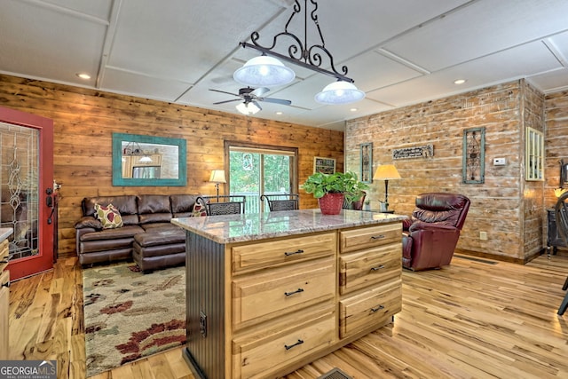 kitchen featuring light stone countertops, light wood finished floors, open floor plan, and hanging light fixtures