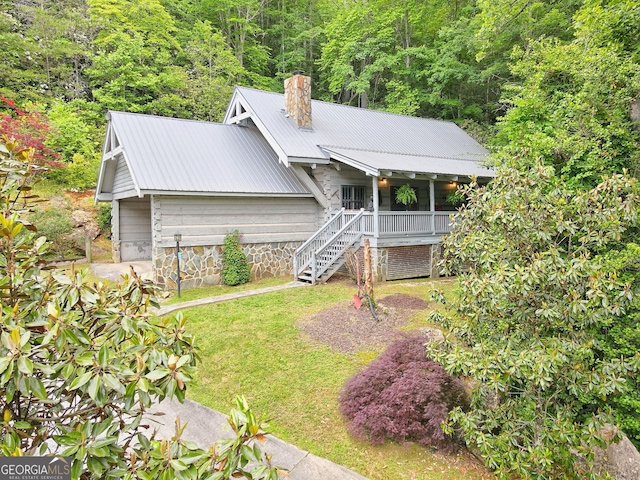 view of front of home with metal roof, a chimney, a front lawn, and stairs