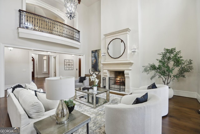 living area with dark wood-style floors, a lit fireplace, baseboards, and a notable chandelier