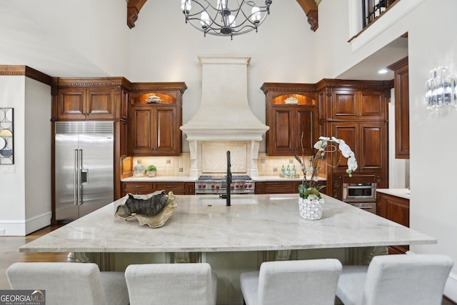 kitchen featuring premium appliances, custom range hood, a breakfast bar, hanging light fixtures, and a kitchen island with sink