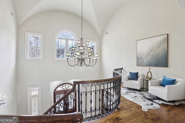 interior space featuring vaulted ceiling, wood-type flooring, an upstairs landing, and an inviting chandelier