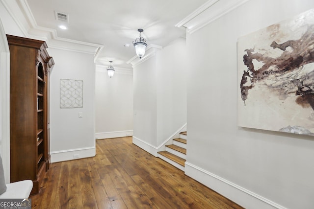 hall with dark wood-style floors, ornamental molding, visible vents, and baseboards