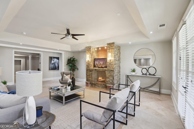 living area with baseboards, visible vents, a raised ceiling, and a stone fireplace