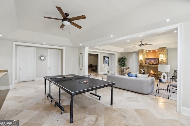 game room featuring recessed lighting, a ceiling fan, baseboards, a lit fireplace, and a tray ceiling