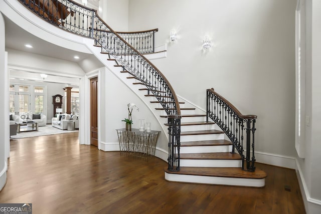 stairway featuring baseboards, a towering ceiling, ornate columns, and wood finished floors