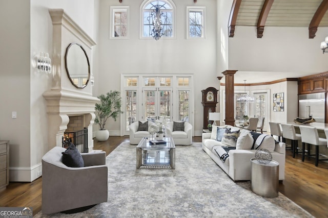 living area with decorative columns, dark wood-style flooring, an inviting chandelier, a fireplace, and beam ceiling