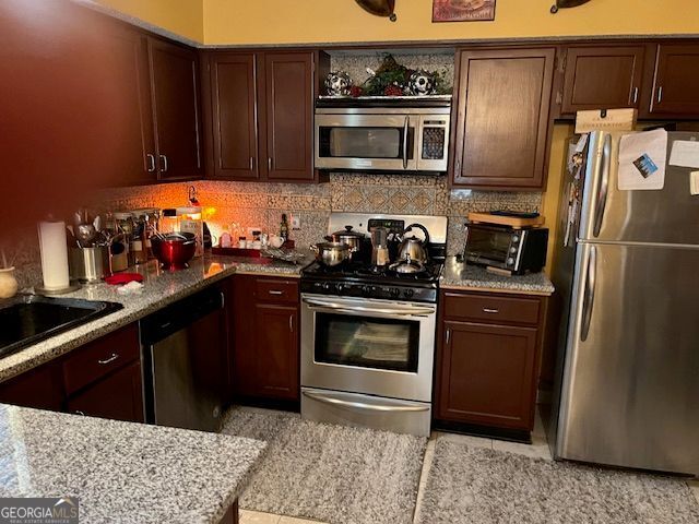 kitchen with a toaster, tasteful backsplash, appliances with stainless steel finishes, a sink, and light stone countertops