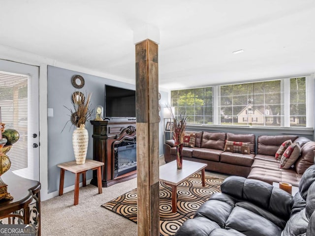 living area featuring light carpet, a glass covered fireplace, and decorative columns