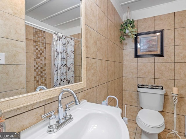 bathroom with toilet, curtained shower, a sink, and tile walls