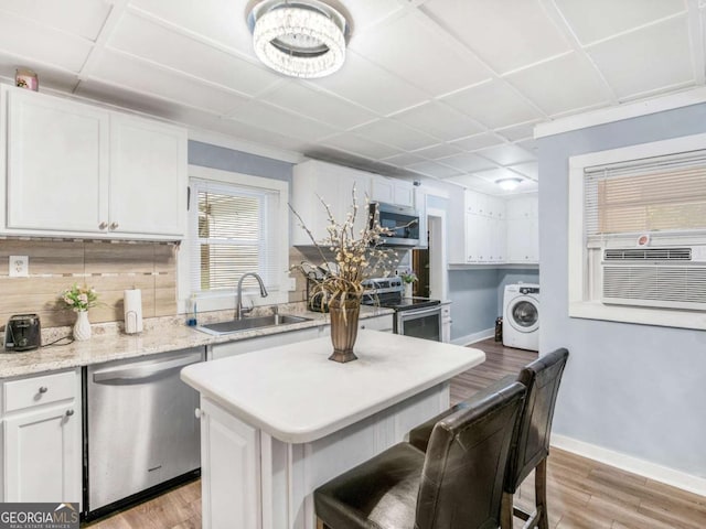 kitchen featuring appliances with stainless steel finishes, washer / dryer, a sink, and white cabinetry