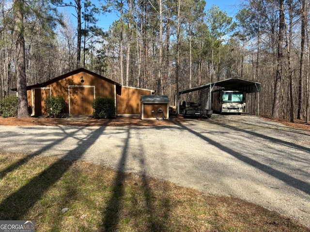 view of side of home featuring gravel driveway, an outdoor structure, and a detached carport