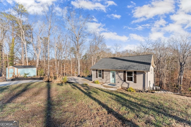 view of front of property featuring driveway, a storage shed, roof with shingles, an outdoor structure, and a front yard