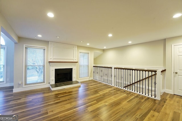 unfurnished living room featuring baseboards, a fireplace with raised hearth, wood finished floors, and recessed lighting