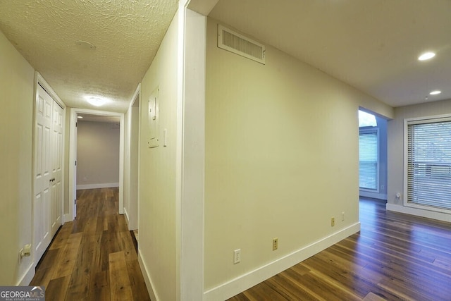 hall with dark wood-type flooring, visible vents, a textured ceiling, and baseboards