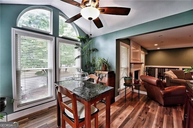 dining space featuring a ceiling fan, lofted ceiling, a fireplace, and wood finished floors