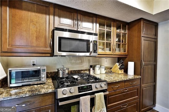 kitchen with a toaster, appliances with stainless steel finishes, glass insert cabinets, and light stone countertops