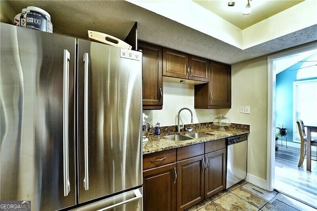 kitchen featuring appliances with stainless steel finishes, dark brown cabinetry, a sink, a textured ceiling, and baseboards