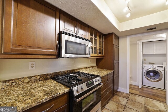 kitchen with stone counters, stainless steel appliances, visible vents, washer / dryer, and baseboards