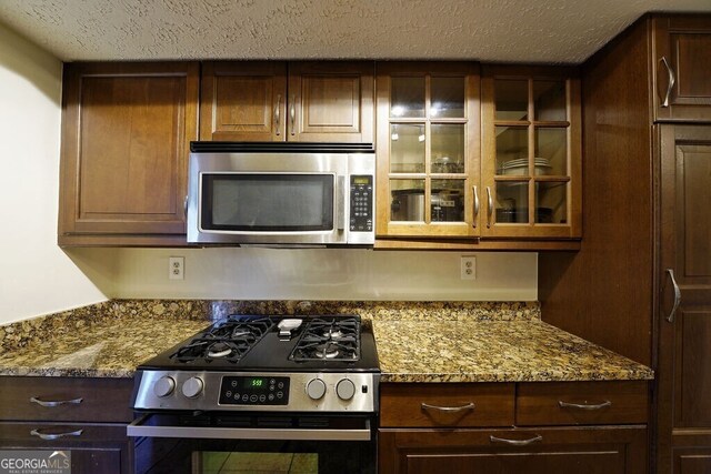 kitchen featuring appliances with stainless steel finishes, stone countertops, glass insert cabinets, and a textured ceiling