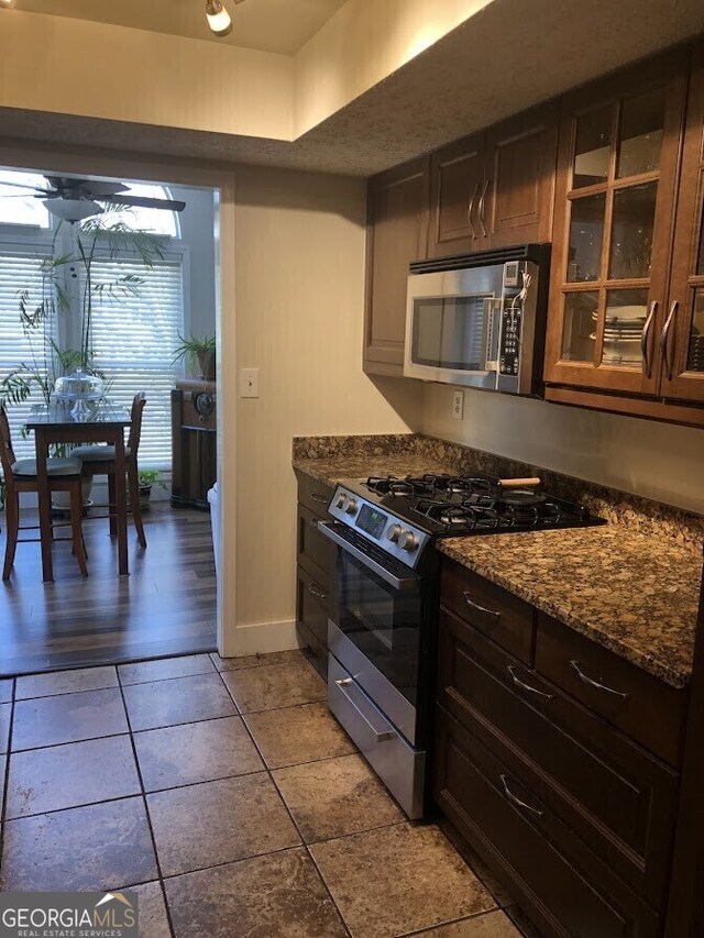 kitchen with light tile patterned floors, glass insert cabinets, stainless steel appliances, and dark stone countertops