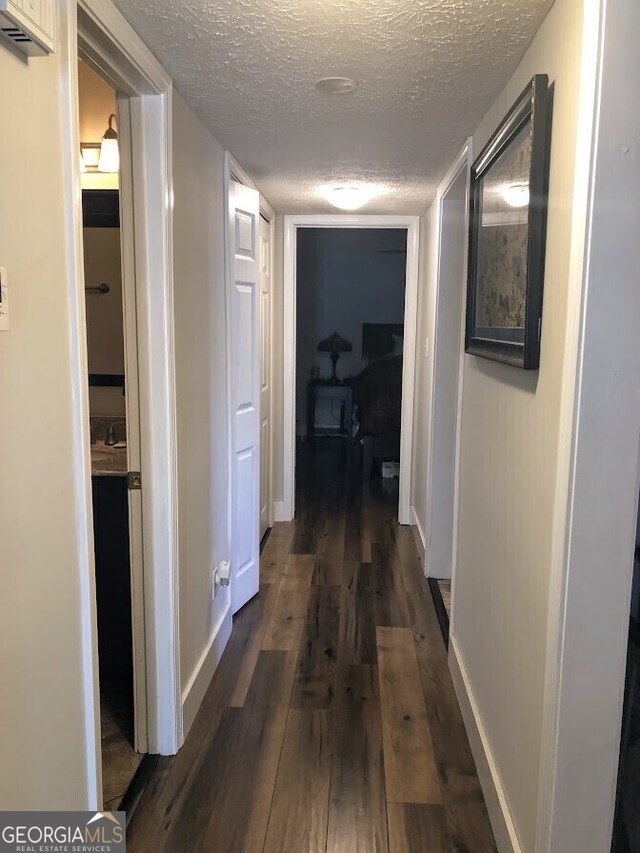 corridor featuring dark wood finished floors, a textured ceiling, and baseboards