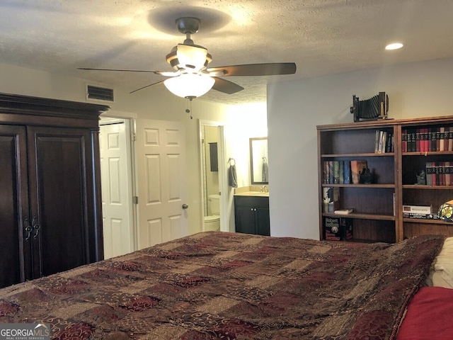 bedroom featuring visible vents, connected bathroom, ceiling fan, a textured ceiling, and a sink