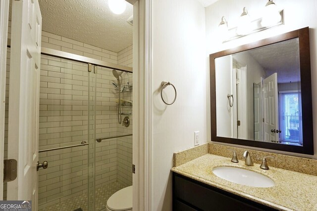 full bathroom featuring toilet, a textured ceiling, a shower stall, and vanity