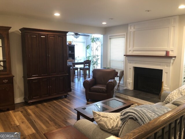 living room featuring a fireplace with raised hearth, dark wood-style flooring, a ceiling fan, and recessed lighting