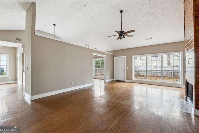 unfurnished living room featuring dark wood-style flooring, a fireplace, lofted ceiling, visible vents, and ceiling fan