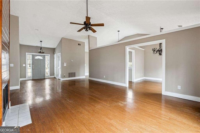 unfurnished living room with ceiling fan with notable chandelier, wood finished floors, visible vents, and baseboards