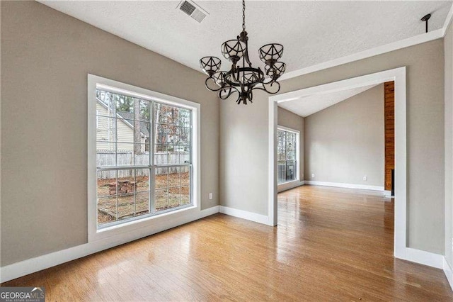 unfurnished dining area with light wood finished floors, baseboards, visible vents, lofted ceiling, and an inviting chandelier