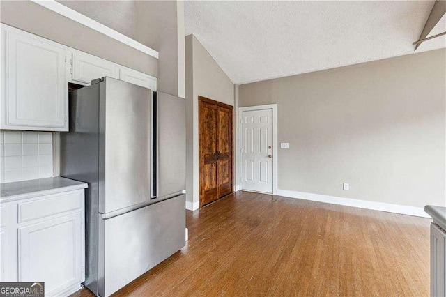 kitchen with lofted ceiling, light countertops, freestanding refrigerator, white cabinetry, and light wood-type flooring