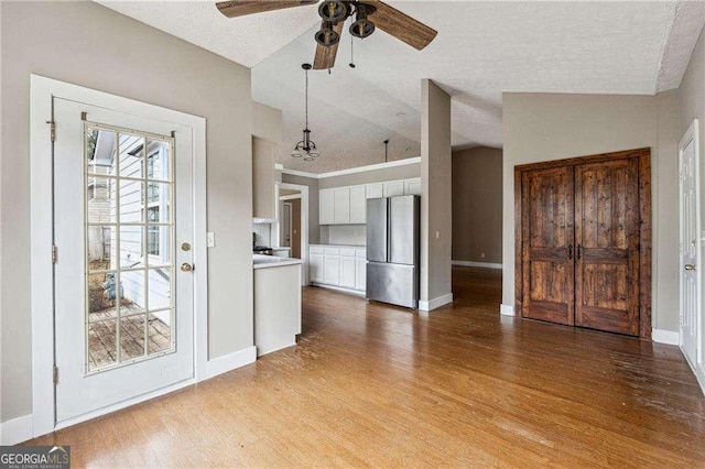 kitchen with white cabinets, light countertops, freestanding refrigerator, light wood finished floors, and pendant lighting