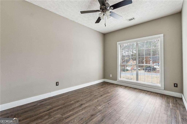 empty room featuring dark wood-style flooring, visible vents, a textured ceiling, and baseboards