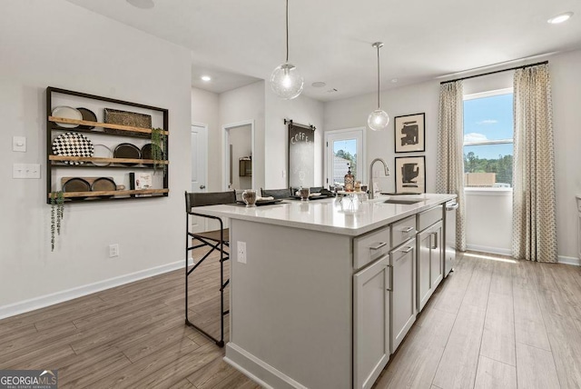 kitchen featuring gray cabinets, light countertops, hanging light fixtures, a kitchen island with sink, and a sink