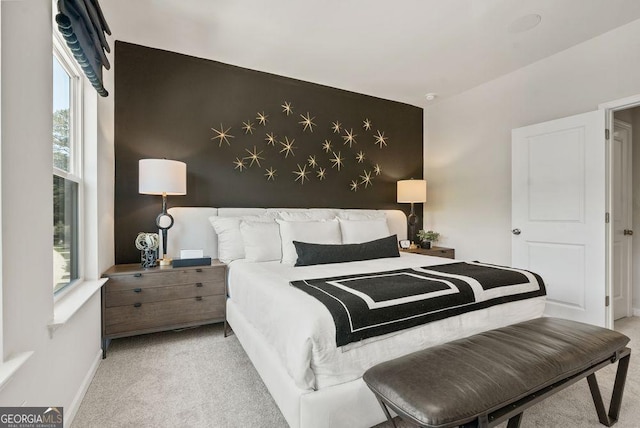 bedroom featuring light carpet, an accent wall, and baseboards