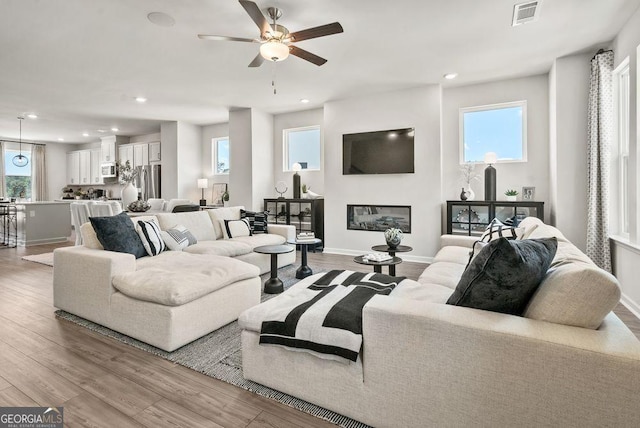 living room featuring light wood-style floors, recessed lighting, visible vents, and a glass covered fireplace