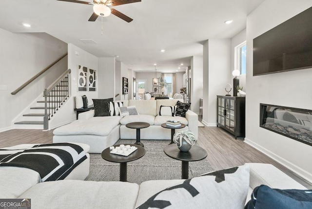 living area featuring stairway, a glass covered fireplace, light wood-style flooring, and baseboards