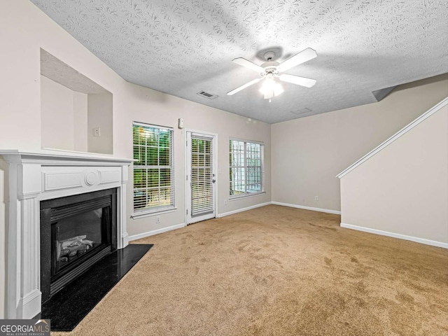 unfurnished living room with carpet, visible vents, a fireplace with flush hearth, ceiling fan, and baseboards