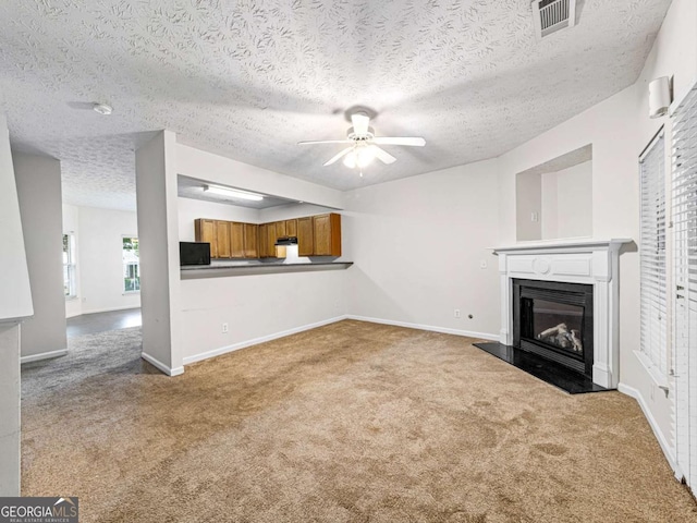 unfurnished living room with baseboards, visible vents, a ceiling fan, a glass covered fireplace, and carpet flooring