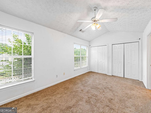 unfurnished bedroom featuring visible vents, lofted ceiling, a textured ceiling, carpet flooring, and two closets