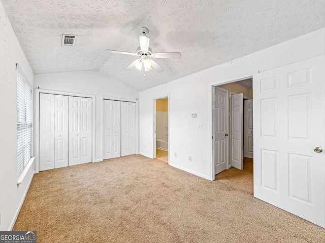 unfurnished bedroom featuring a textured ceiling, lofted ceiling, light carpet, visible vents, and multiple closets