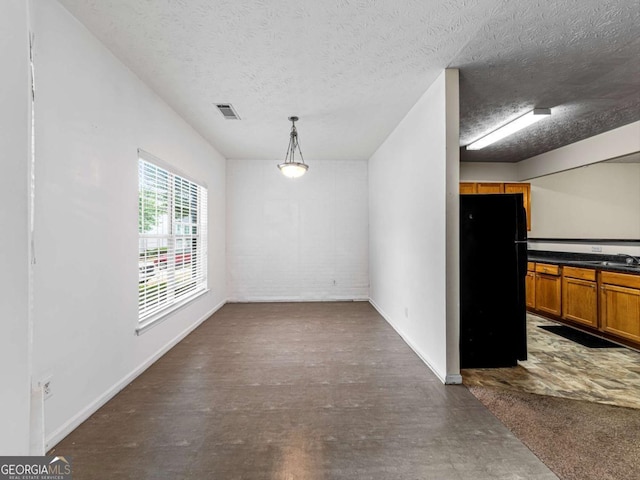 unfurnished dining area featuring baseboards, a textured ceiling, visible vents, and a sink